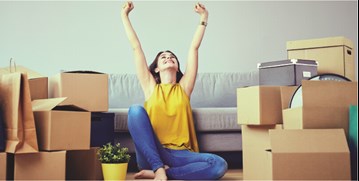 an excited woman with her hands up sitting on the floor surrounded by boxes