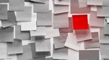 A wall covered in white sticky notes with one red one.