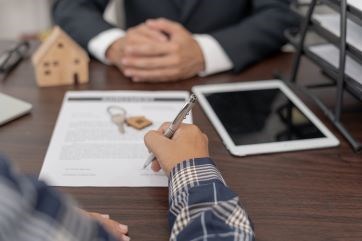 Hands signing a document with a set of keys sitting on it.