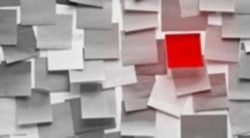 A wall of white sticky notes with one red one.