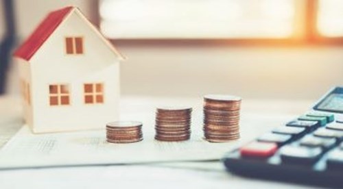 an image of a model house next to a stack of coins and calculator